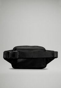 Bolso de cintura negro de nailon con un acabado suave, forma rectangular, bolsillo delantero con cremallera y correa ajustable. Diseño minimalista sin patrones.