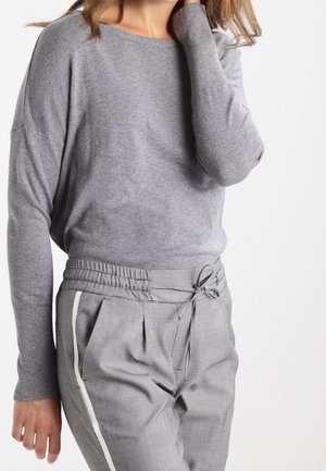 Pull en gris à manches longues avec une coupe décontractée associé à un pantalon en gris à motifs avec une taille à cordon de serrage et un détail blanc sur le côté.