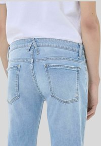 Jeans in denim azzurro con vita media, design a cinque tasche e dettagli di cucitura sottili, visti da dietro.