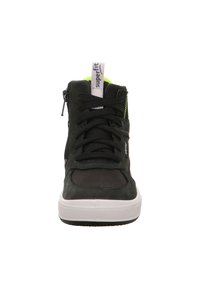 Černé vysoké tenisky s bílou podrážkou, černými tkaničkami, bočním zipem a neonově zeleným polstrováním uvnitř, označené nápisem "superfit" na jazyku.