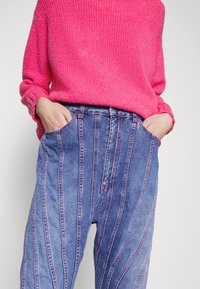 Flauschiger rosa Pullover in Kombination mit blauen, gestreiften Jeanshosen mit kontrastierenden Nähten. Die Hosen besitzen seitliche Taschen und einen lässigen Schnitt.