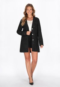 Cardigan nero con un motivo texture, maniche lunghe e tasche frontali. Presenta bottoni lucidi e una vestibilità comoda, indossato sopra una maglietta leggera.