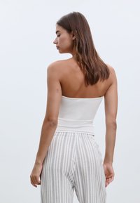 Bílý bezramínkový top vyrobený z hladkého materiálu, přiléhavý střih. Nosit s šedými a bílými pruhovanými pyžamovými kalhotami s elastickým pasem.
