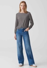 Zwart-wit gestreepte langemouwtop met een ronde kraag, gecombineerd met lichtblauwe wijde jeans en witte sneakers.