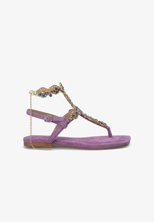 Sandale en suede violet avec une bride en T ornée de bijoux, présentant une chaîne décorative en or et une semelle plate. Bride de cheville ajustable pour un bon ajustement.