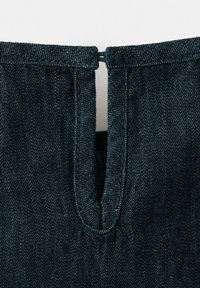Gros plan sur un tissu en denim bleu foncé avec une fente verticale et un bord supérieur cousu avec une double surpiqûre, montrant la texture détaillée et la couture.