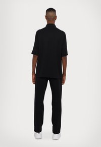 Svart kortermet polo med en avslappet passform, kombinert med matchende svarte bukser. Glatt tekstur, minimal detaljering og rett silhuett.