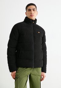 Schwarze Corduroy-Puffjacke mit hohem Kragen, Reißverschluss und kleinem Logo. Sie verfügt über gesteppte Bereiche und seitliche Taschen.