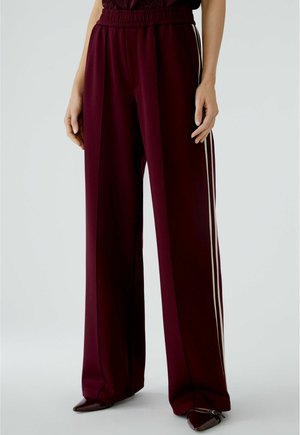 Pantalons bourgogne avec une taille élastique, dotés de deux rayures latérales blanches contrastantes et d'une coupe large. Texture de tissu lisse.