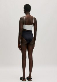 Hooggesneden bikini onderstuk in marineblauw, gecombineerd met een witte crop top. Het materiaal is glad met verstelbare bandjes en een minimalistisch ontwerp.