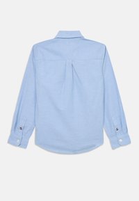 Camisa de mangas longas azul clara com colarinho abotoado, plissado nas costas e punhos abotoados, apresentando um pequeno logotipo no braço.
