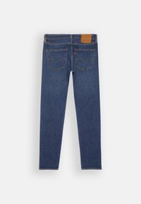 Vaqueros de denim azul ajustados con cinco bolsillos, costura en contraste y una etiqueta de cintura de cuero marrón. La tela tiene una textura suave.