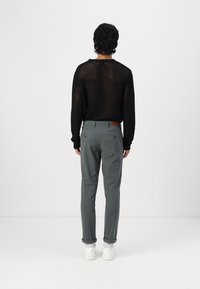 Svart mesh-genser med lange ermer, kombinert med lysegrå slim-fit bukser og hvite joggesko. Merkbare detaljer inkluderer knappedetaljer på baklommene.