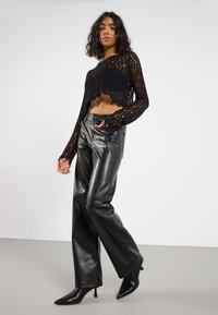 Maglione corto in crocchettato nero a maniche lunghe, abbinato a pantaloni wide-leg in pelle nera lucida e décolleté a punta.