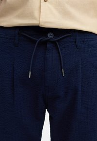 Marineblå shorts med struktur og snoreliv. Stof med en subtil, mønstret tekstur. Har lommeåbninger i begge sider.
