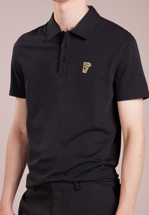 Polo nera a maniche corte con colletto e tre bottoni, con un piccolo emblema dorato sul petto sinistro.