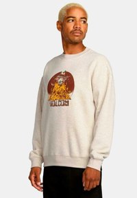 Sudadera crewneck de color beige claro con un estampado gráfico de una montaña y llamas, que presenta la palabra "VOLCOM". Tejido texturizado con puños acanalados.