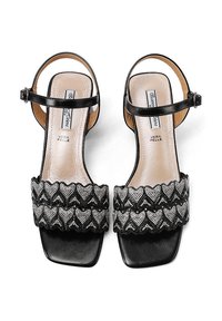 Sandalias de tacón negro con puntera cuadrada, que presentan una correa texturada y ondulada adornada con detalles plateados y una correa ajustable en el tobillo.