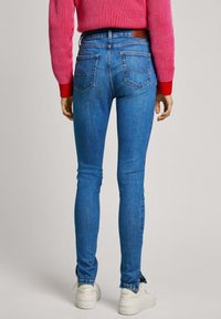 Úzké modré džíny s hladkou texturou a designem na pět kapes, s pasem v polovině výšky a jemnými švy. V kombinaci s bílými teniskami.