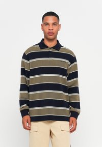 Poloshirt met lange mouwen in olijfgroen en marineblauwe strepen met witte accenten. Voorzien van een kraag en een sluiting met twee knopen, gewafelde manchetten.