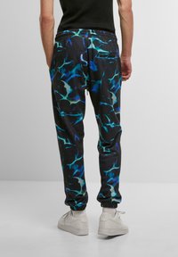 Sorte joggers med blå og grønne abstrakte mønstre, elastisk talje og ankelmanchetter; parret med hvide sneakers.