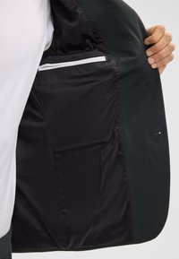 Giacca nera con un rivestimento interno liscio, dotata di una tasca con zip e cuciture a contrasto lungo i bordi.
