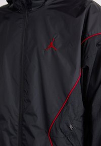 Sort zip-jakke med rød piping og et rødt broderet Jumpman-logo på brystet.