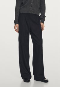 Černé pruhované kalhoty vyrobené z lehkého materiálu, s volným střihem a elastickým pasem. V kombinaci s tmavě šedým cardiganem.