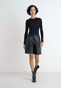 Zwarte long-sleeve top, gecombineerd met hoge zwarte leren shorts en zwarte enkellaarsjes met gespen. Gladde textuur en een getailleerde pasvorm.
