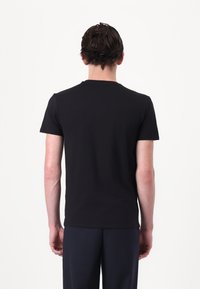 Juodas prigludęs marškinėliai su apvalia iškirpte ir trumpomis rankovėmis. Lygus medvilnės audinys, minimalistinis dizainas ir be siūlių konstrukcija nugarinėje dalyje.