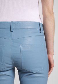 Pantaloni in ecopelle blu chiaro con una texture liscia, dotati di una vita, passanti per cintura e due tasche posteriori con dettagli di cucitura.