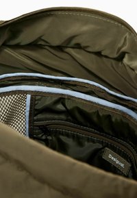 Intérieur de sac vert olive avec plusieurs compartiments, poche en maille et texture lisse, avec une étiquette indiquant "Desigual". Fermeture éclair.