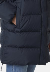 Chaqueta acolchada de color azul marino con un diseño de acolchado, que cuenta con un gran bolsillo, textura suave y un cierre de cremallera en el dobladillo inferior.