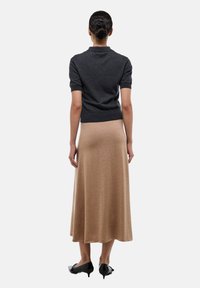 Un pull gris foncé à manches courtes associé à une longue jupe fluide beige. Des escarpins noirs à bout pointu viennent compléter la tenue. Textures lisses dans l'ensemble.
