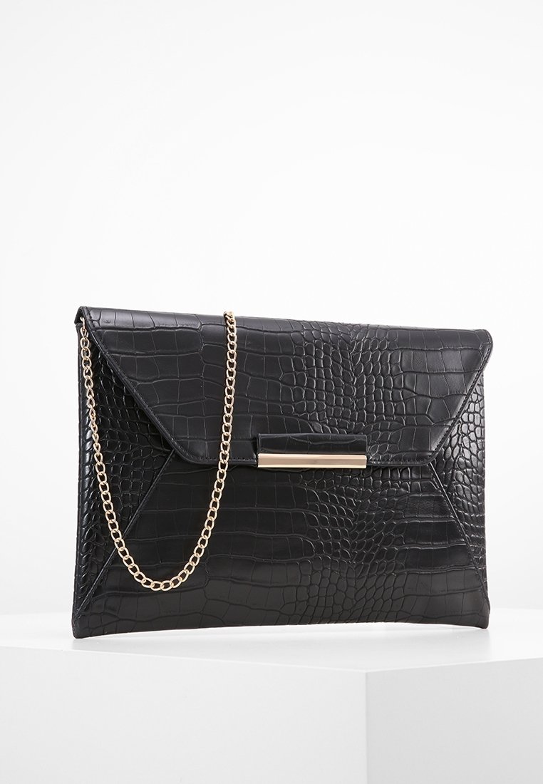 Pochette en cuir noir à texture crocodile avec une chaîne dorée et un fermoir rectangulaire doré sur une surface blanche.