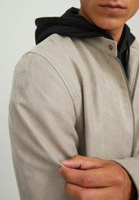 Beige suede jacket with a zip closure, structured shoulders, and a black hooded layer underneath, showcasing a smooth texture.