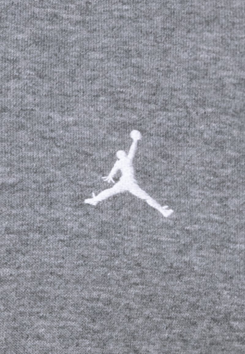 Un tissu de sweat-shirt gris présentant un logo Jumpman blanc brodé, placé au centre, mettant en valeur une texture lisse et un design sportif.