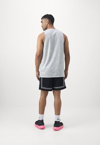 Camiseta sin mangas de malla gris, pantalones cortos negros con ribete blanco y zapatos negros con suelas rosas. Vista desde atrás, mostrando la textura del tejido y ajuste.