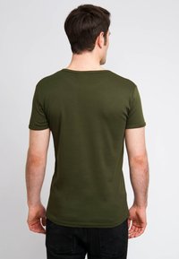 Camiseta de manga corta en verde oliva, diseño ajustado con cuello redondo y textura suave. Vista desde la espalda, combinada con jeans oscuros.