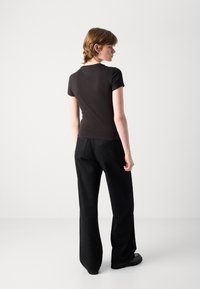 Chemise noire à manches courtes avec un design ajusté. Portée avec un pantalon noir à motifs de points. Texture notable et couleur unie.