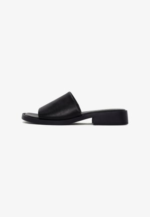 Sandale mule en cuir noir avec bout ouvert, large bride, talon carré bas et semelle plate, vue de côté sur fond blanc.