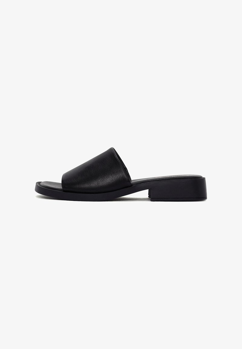 Sandale mule en cuir noir avec bout ouvert, large bride, talon carré bas et semelle plate, vue de côté sur fond blanc.