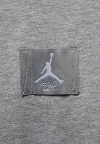 Grått textil med en slät yta har en grå patch som visar en vit Jumpman-logotyp och texten "Flight" i stiliserad font.