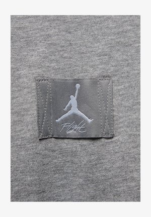Grått textil med en slät yta har en grå patch som visar en vit Jumpman-logotyp och texten "Flight" i stiliserad font.