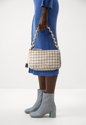 Personne en robe bleu côtelée tenant un sac à main beige en tweed avec anse chaîne, portant des bottines grises claires à talons blocs.