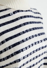 Knit sweater featuring a high collar, white and navy stripes, and sequins interspersed in a horizontal pattern. Soft texture, casual design.
