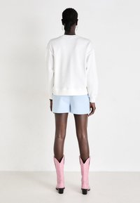 Hvit hettegenser med lange ermer, kombinert med lyseblå shorts og rosa cowboystøvler med spisse tå og svarte hæler.