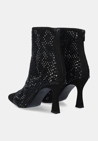 Botines negros de tobillo con parte superior trenzada, puntera afilada y un tacón de 5 cm. Con cremallera en la parte trasera para ponérselos con facilidad. Textura suave.