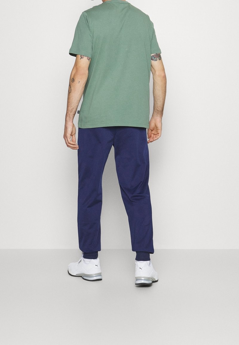 T-shirt vert à manches courtes, associé à un pantalon de jogging marine et des chaussures de sport blanches. Il présente un ourlet droit et une coupe décontractée.
