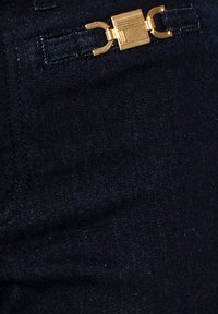 Jeans de mezclilla oscura con un cierre en tono dorado en la cintura. Textura suave con detalles de costura sutiles. Diseño ajustado clásico.